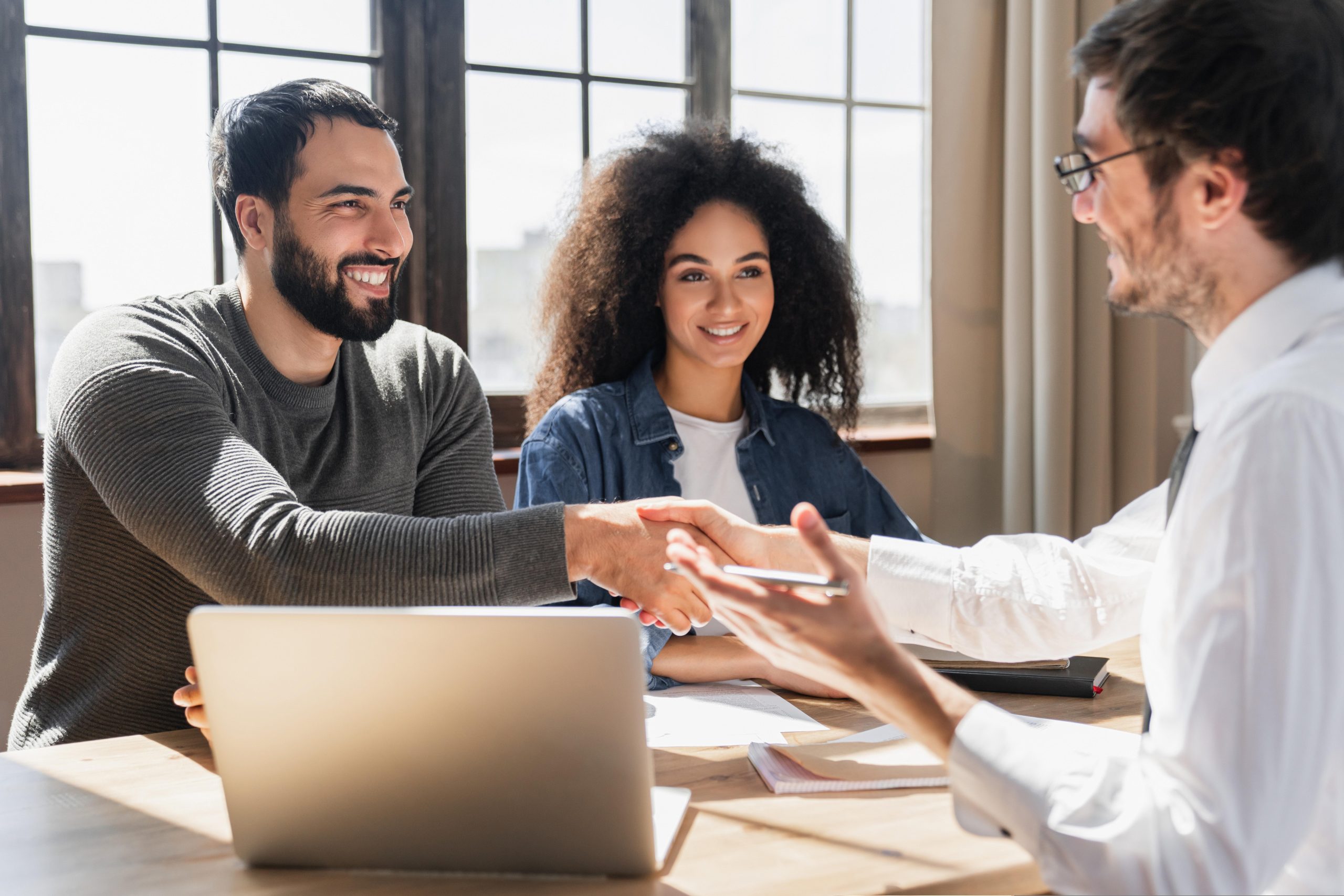 A couple shaking hands with a professional at a meeting table.